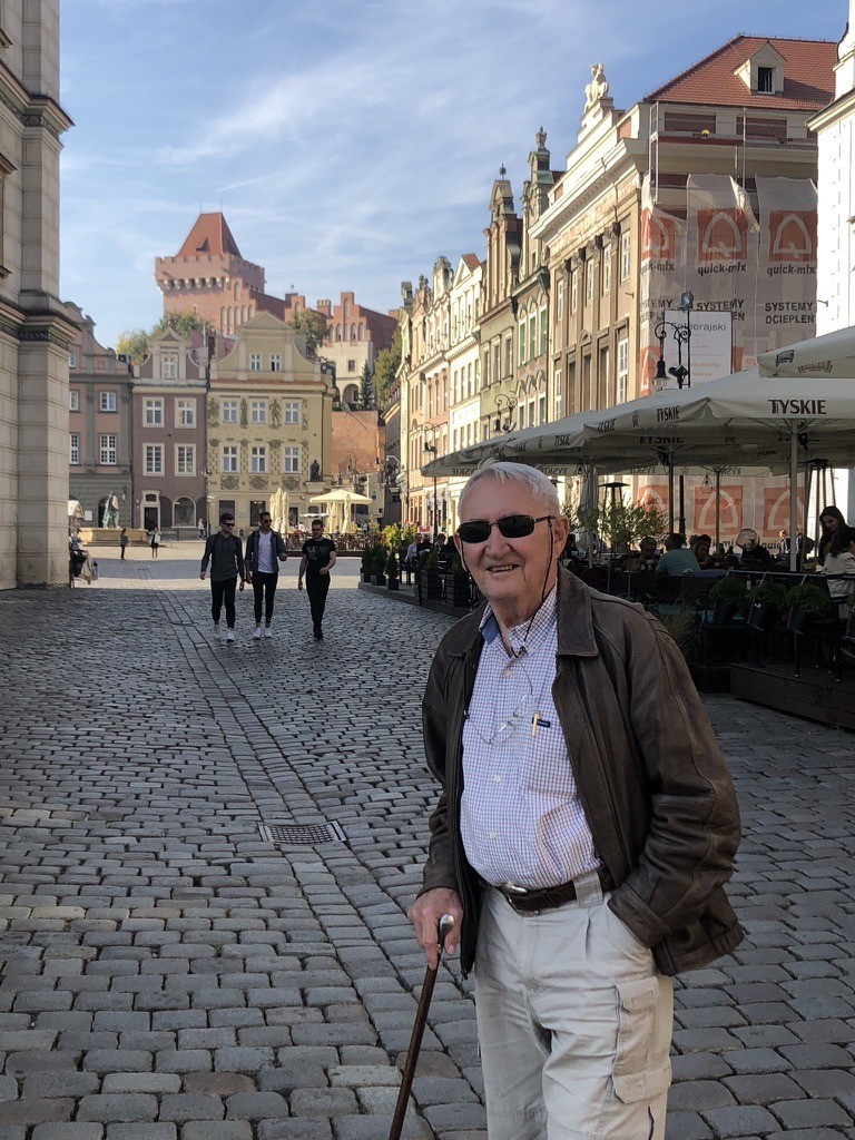Stan Siedlecki na Starym Rynku w Poznaniu — słoneczny dzień, kamienna nawierzchnia, historyczne fasady kamienic w tle, w ręce trzymający laskę